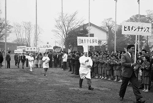 選手村閉村式でコックの派遣元であった「日本ホテル協会」のプラカードを掲げて行進する食堂勤務者（1964年10月）
