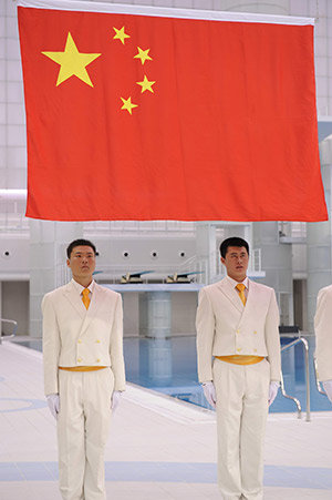 中国国旗の下で直立不動の姿勢を取るスタッフ。水泳会場にて 